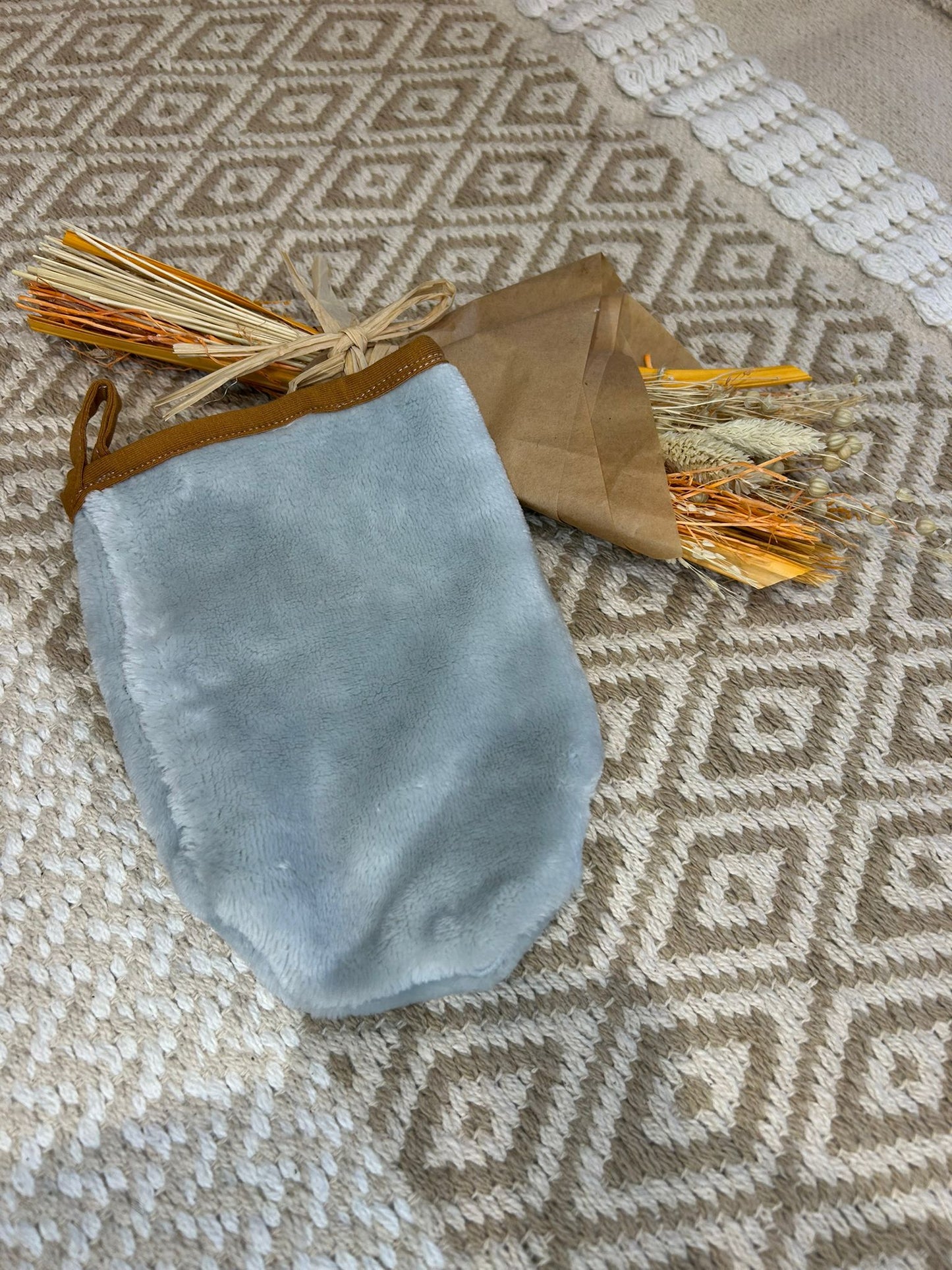 gant de toilette doux démaquillant, gris sur un tapis beige et fleur sécher