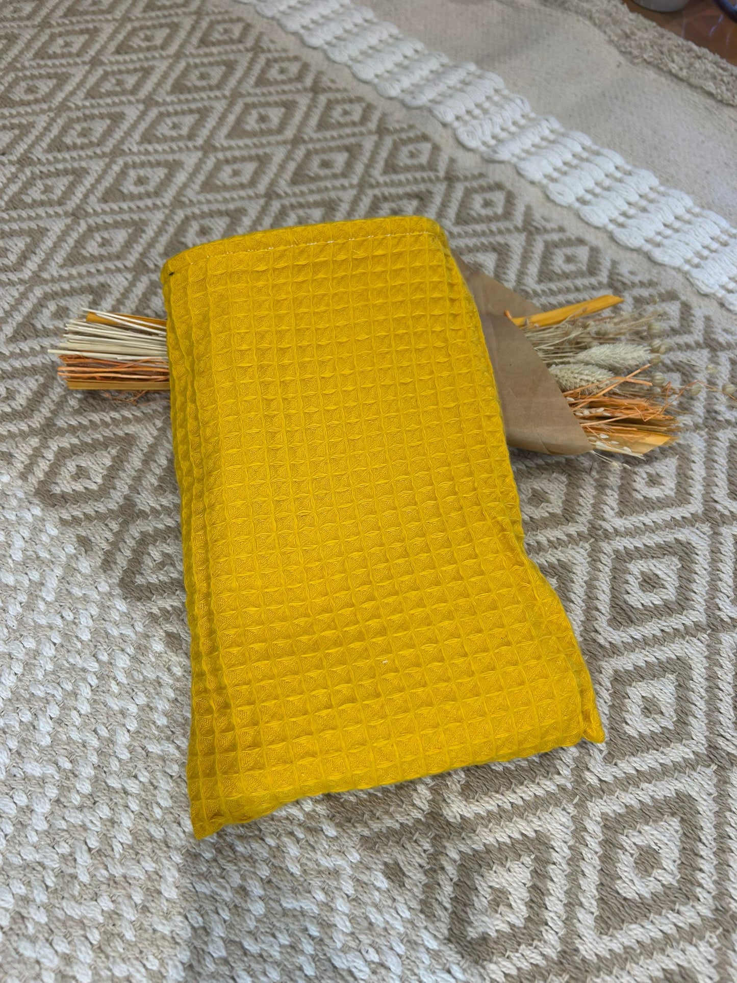 gant de toilette jaune avec filet blanc, sur un tapis beige avec des fleurs sécher