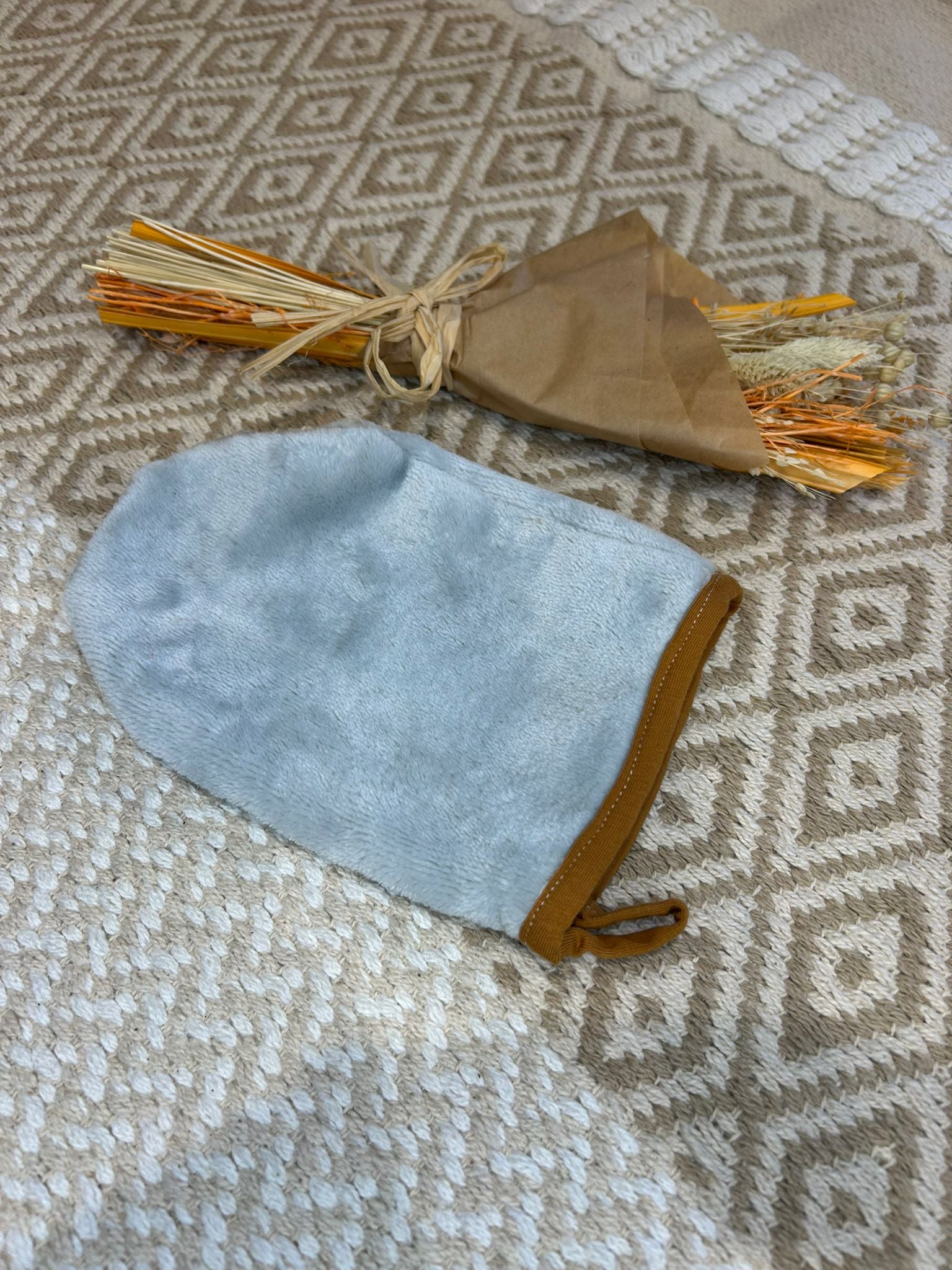 gant de toilette doux démaquillant, gris sur un tapis beige et fleur sécher 