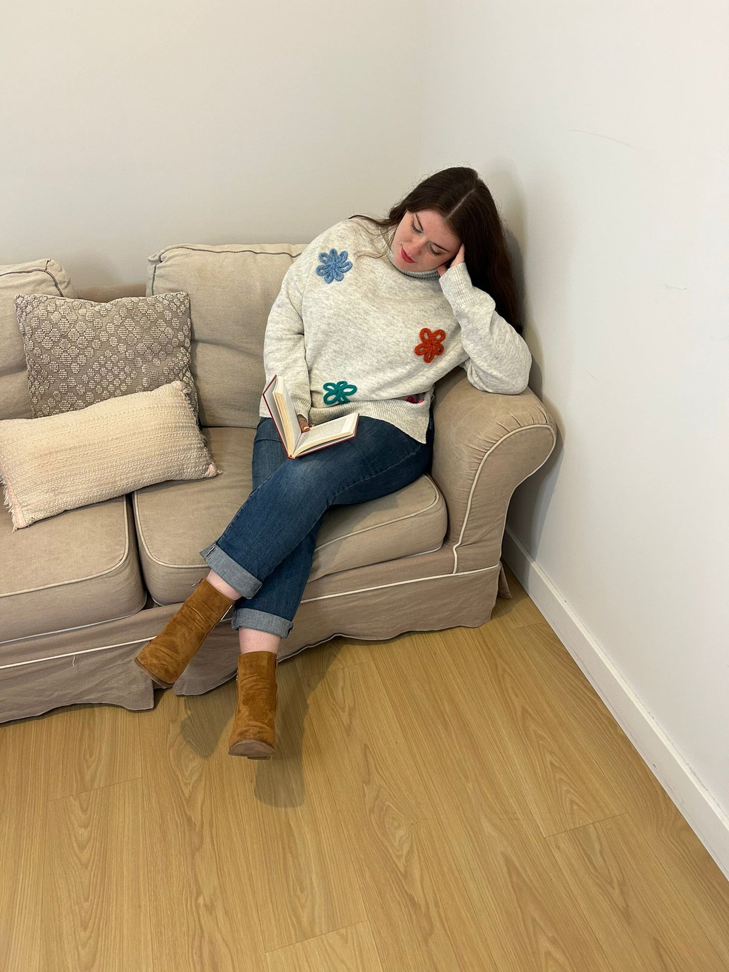 Pull blanc col roulé à fleurs, femme lisant son livre sur un canapé blanc 