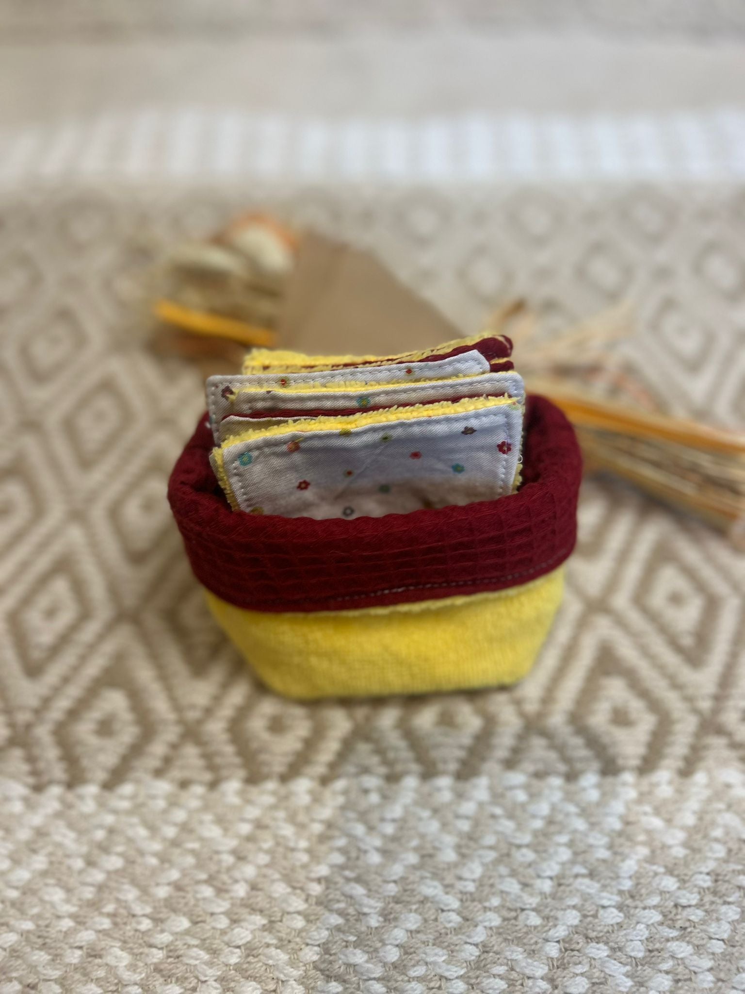 carré de coton démaquillante lavable jaune et bordeaux en coton et nid d'abeille, sur une tapis 


