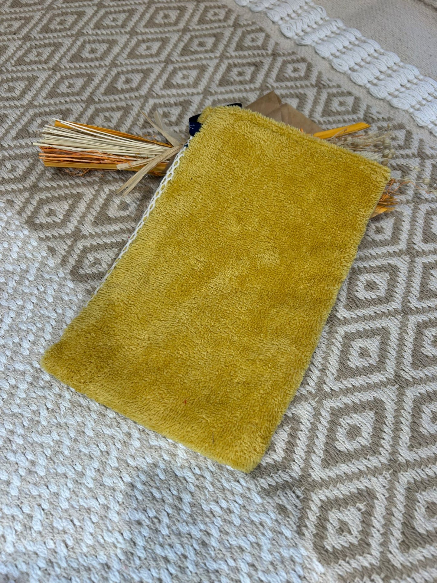 gant de toilette jaune avec filet blanc, sur un tapis beige avec des fleurs sécher 