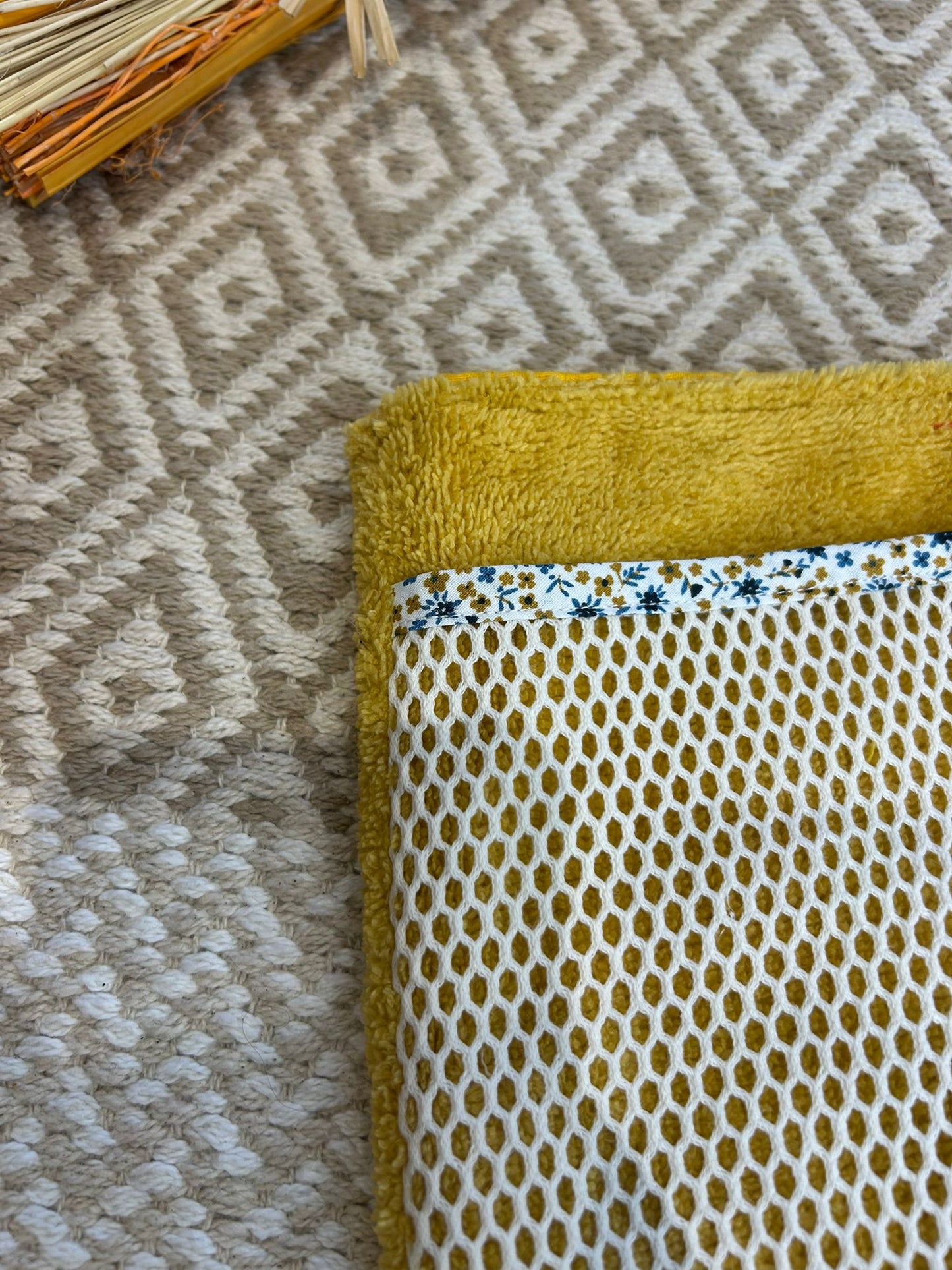 gant de toilette jaune avec filet blanc, sur un tapis beige avec des fleurs sécher 