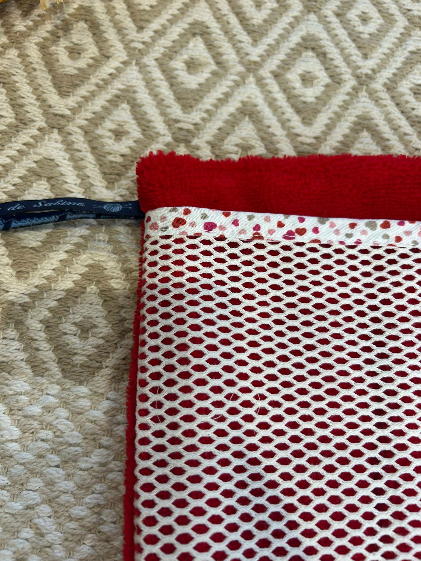 gant de toilette rouge, filet blanc et coeur sur un tapis beige et un bouquet de fleurs sécher 