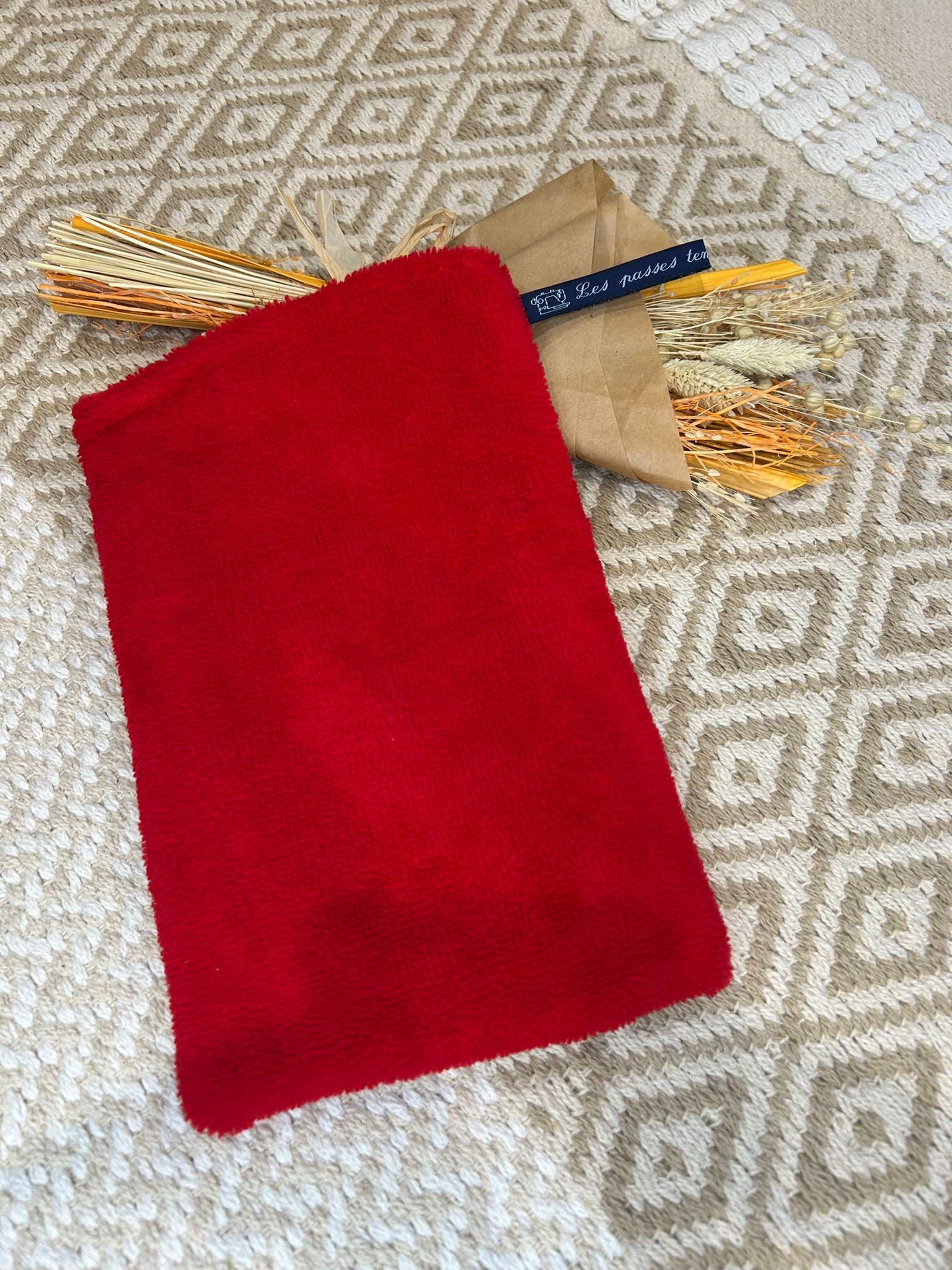 gant de toilette rouge, filet blanc et coeur sur un tapis beige et un bouquet de fleurs sécher 