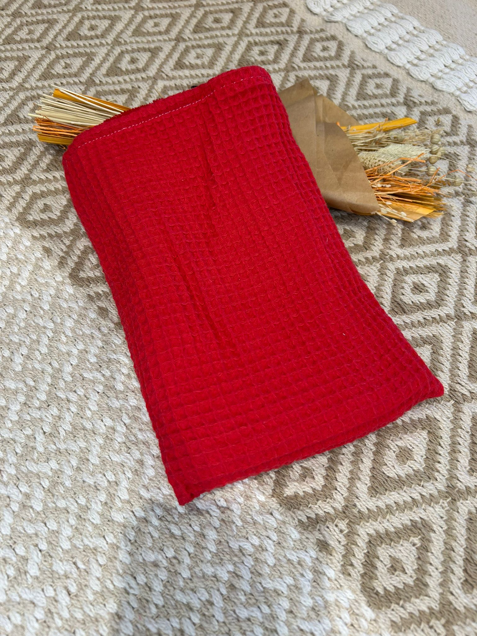 gant de toilette rouge, filet blanc et coeur sur un tapis beige et un bouquet de fleurs sécher 