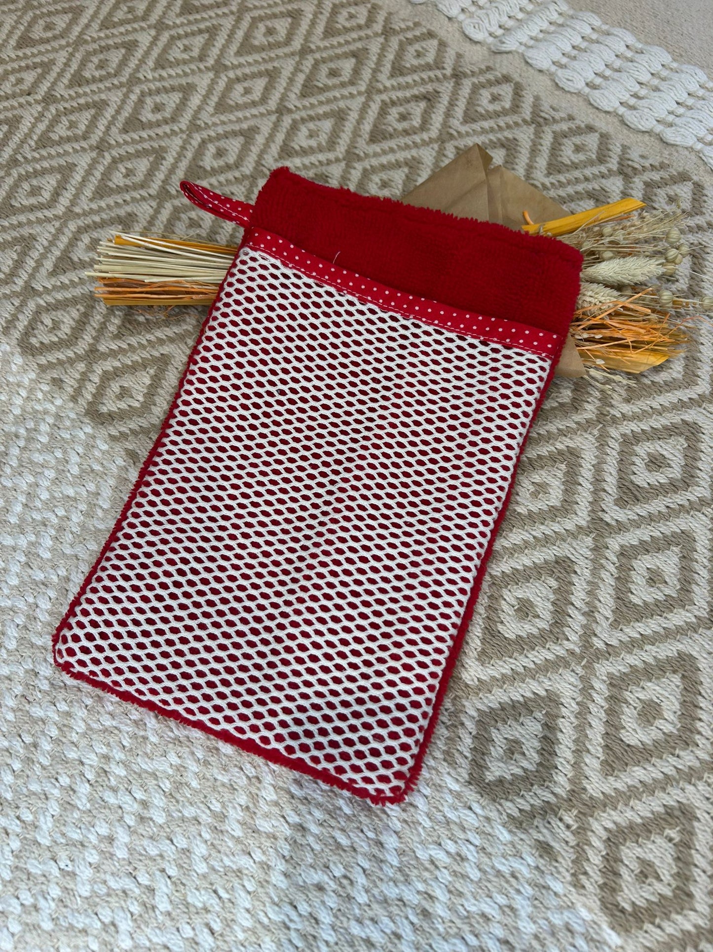 gant de toilette démaquillant rouge avec filet blanc à pois, sur un tapis beige et des fleurs