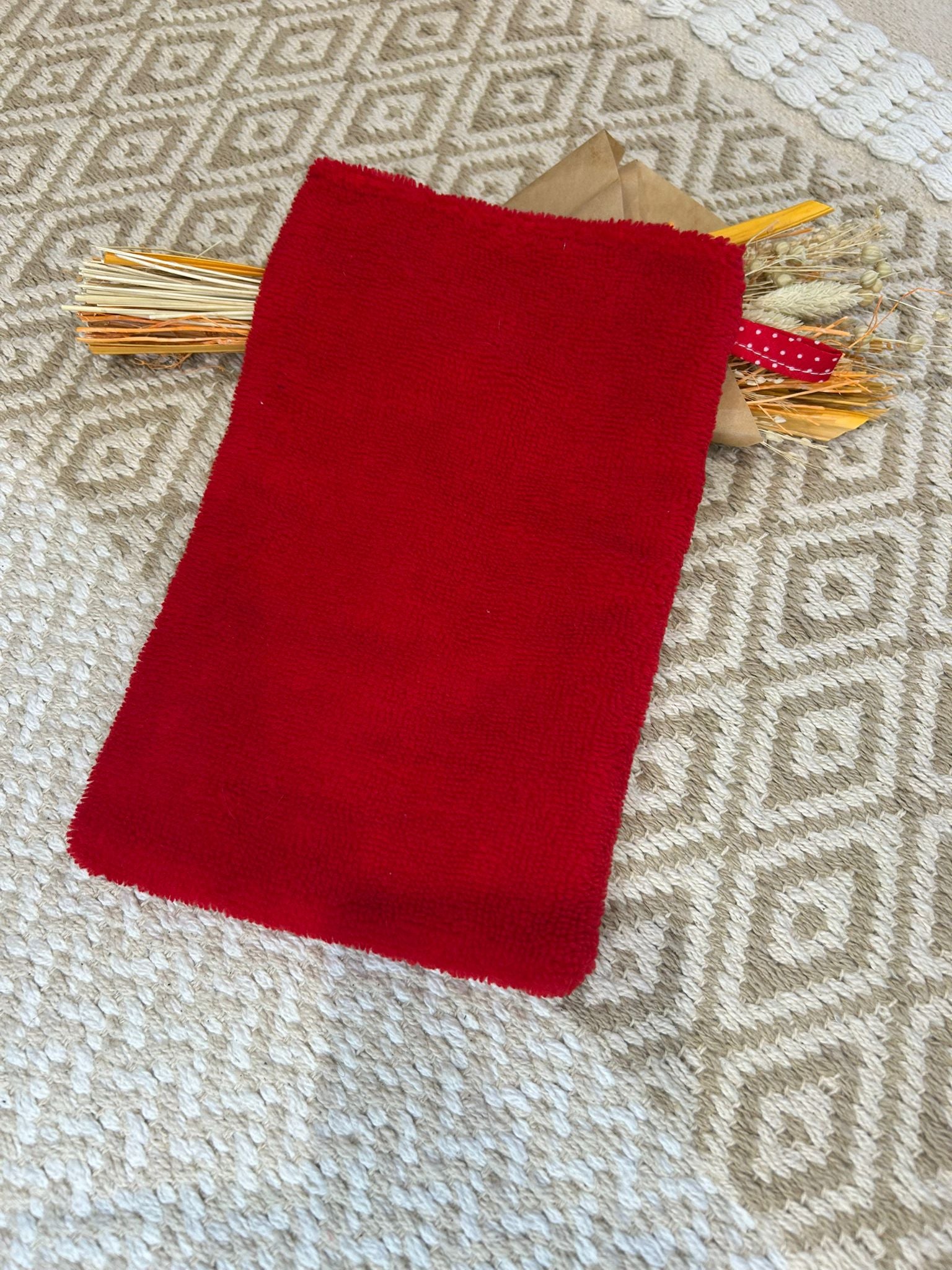 gant de toilette démaquillant rouge avec filet blanc à pois, sur un tapis beige et des fleurs