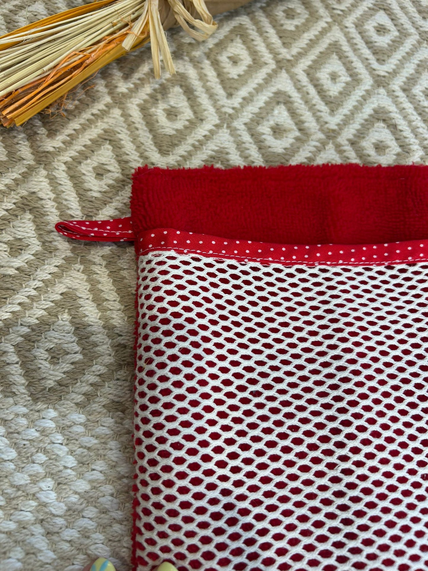 gant de toilette démaquillant rouge avec filet blanc à pois, sur un tapis beige et des fleurs