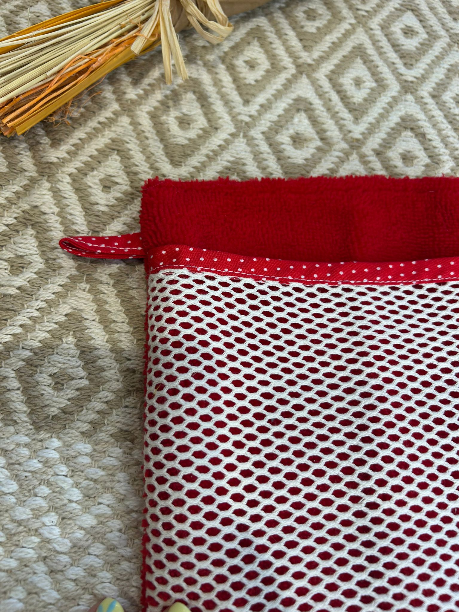 gant de toilette démaquillant rouge avec filet blanc à pois, sur un tapis beige et des fleurs