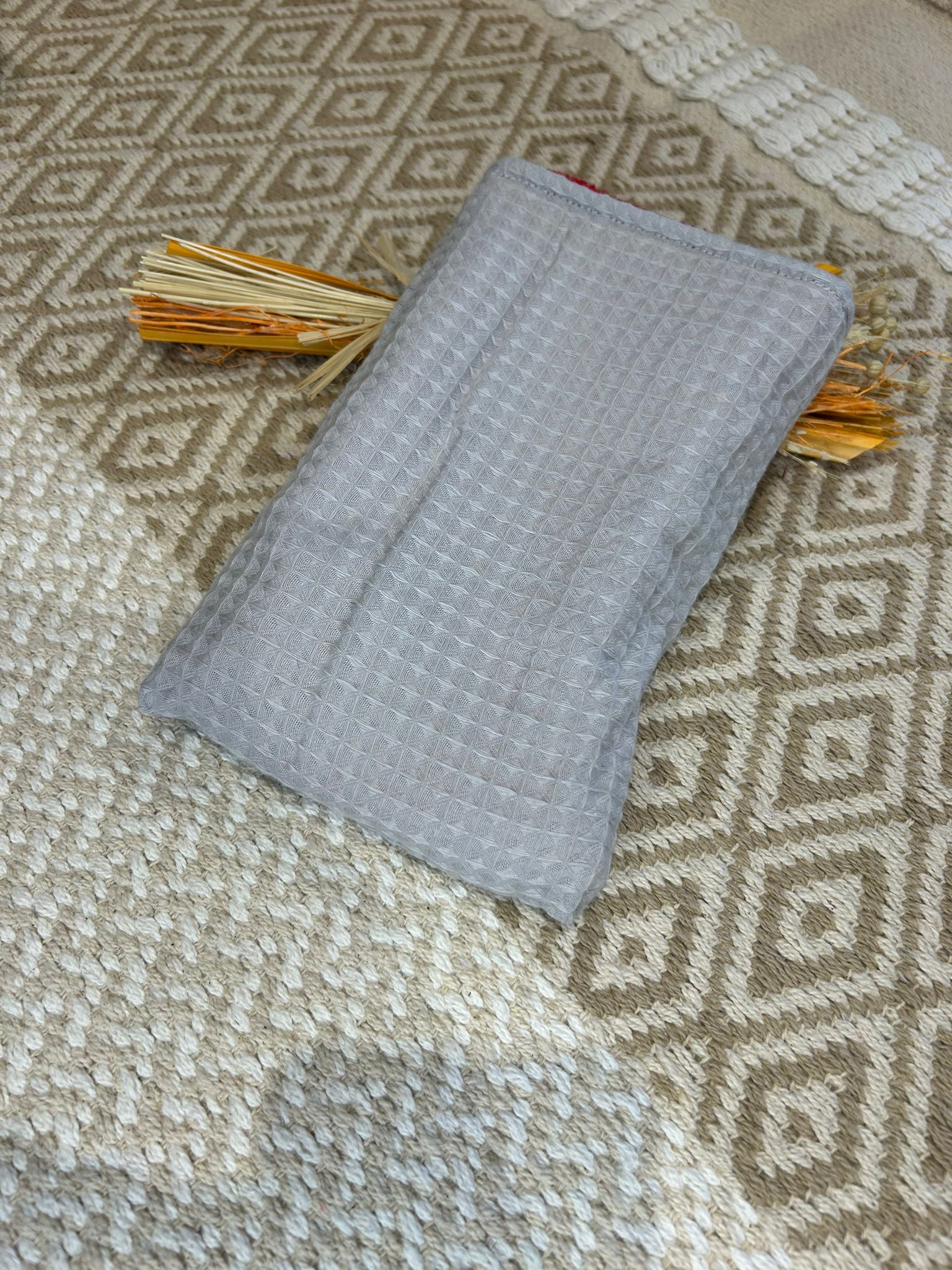 gant de toilette démaquillant gris avec filet blanc à pois, sur un tapis beige et des fleurs